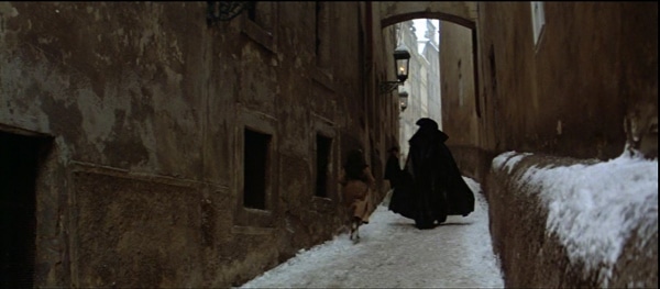 screenshot from the film Amadeus of a cloaked man walking down a narrow snowy street