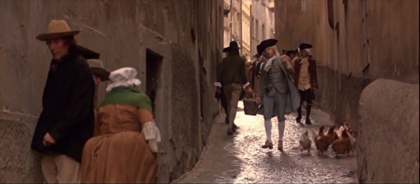 screenshot from the film Amadeus of Mozart walking down a cobblestone street