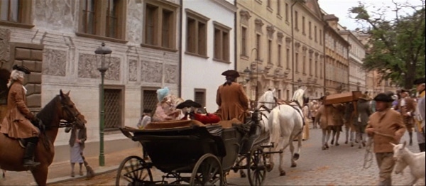 a screenshot from the movie Amadeus of a horse drawn carriage going down a street