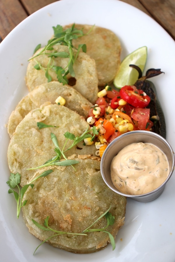 a plate of fried green tomatoes with corn salad and sauce