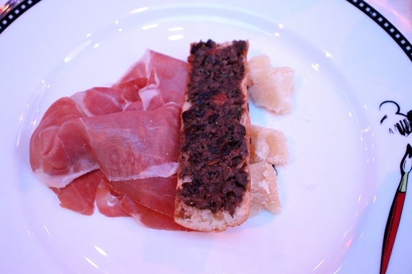 toasted bread with olive tapenade, serrano ham, and cheese on a plate