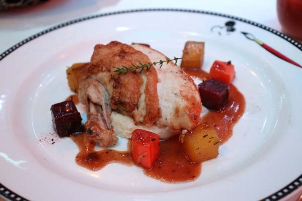 chicken breast on a plate surrounded with roasted vegetables and sauce