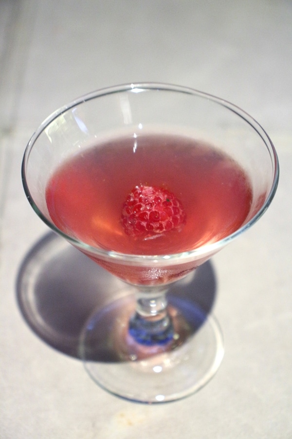 a small pink cocktail garnished with a raspberry