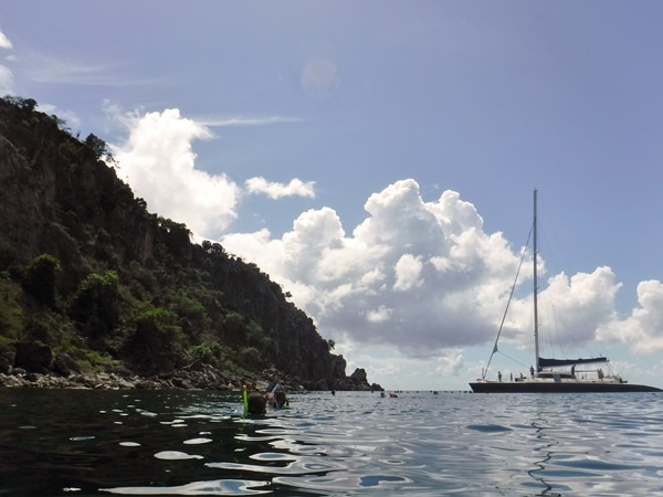 a catamaran in the distance with snorkelers in the water nearby