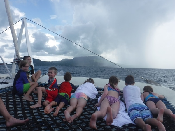 A group of people sitting in a catamaran looking at a storm in the distance