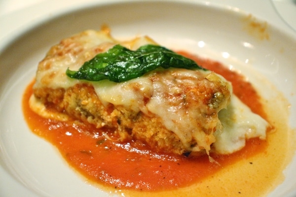 eggplant rollatini topped with cheese and basil on a white plate