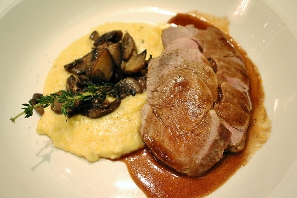 sliced pork tenderloin with brown sauce, and polenta with mushrooms on a white plate