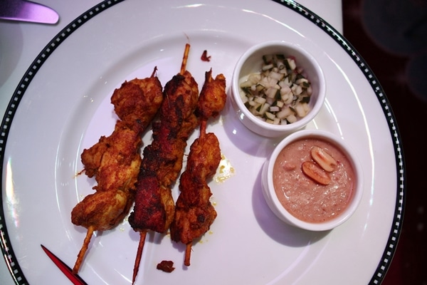 skewered chicken with sauce on the side on a white plate