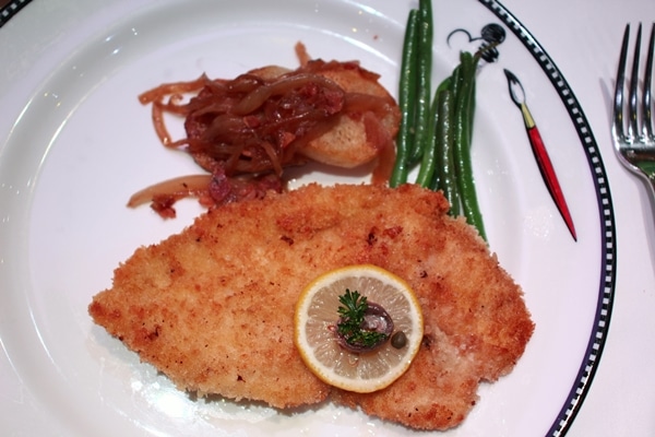 chicken schnitzel with lemon and green beans on a white plate