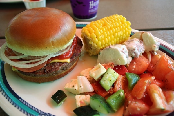 burger, corn on the cob, and salads on an oval plate