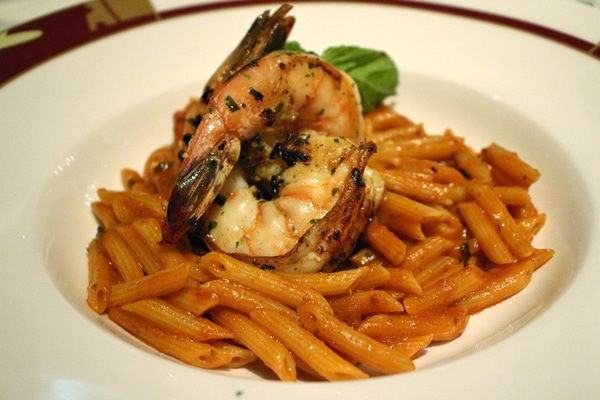 a bowl of penne pasta with tomato sauce, and grilled jumbo shrimp