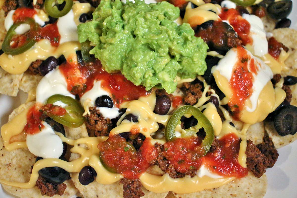 Closeup of nachos with cheese sauce, salsa, black beans, olives, ground beef, sour cream, and guacamole.