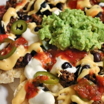 Close up of loaded nachos with cheese sauce, salsa, black beans, meat, olives, and guacamole.