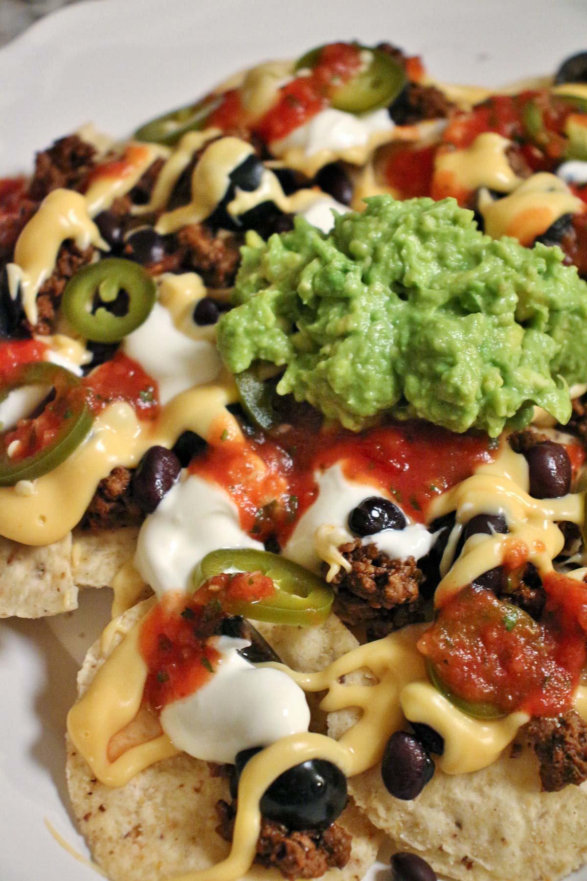 Close up of loaded nachos with cheese sauce, salsa, black beans, meat, olives, and guacamole.