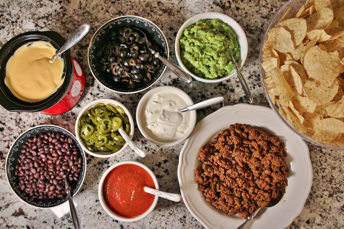 Bowls filled with various toppings for nachos arranged on a granite countertop.