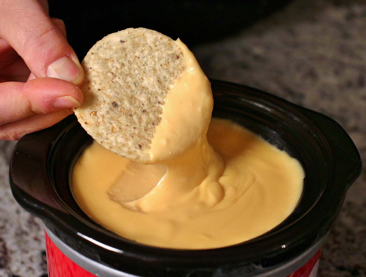 A tortilla chip dipped in homemade nacho cheese sauce (queso).