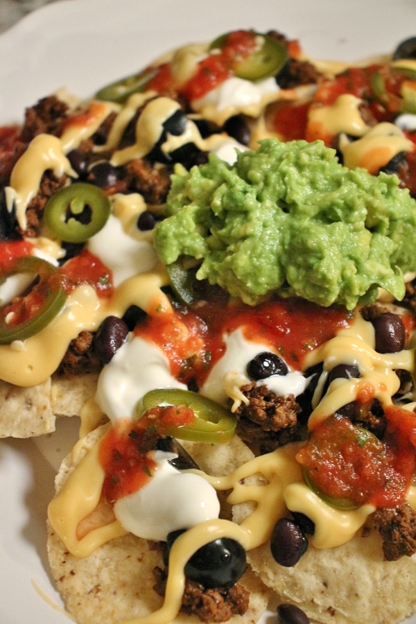 Plate of Nachos with Taco Meat, Nacho Cheese Sauce, Guacamole, Salsa, Olives, Beans, Pickled Jalapenos, Sour Cream, and Tortilla Chips