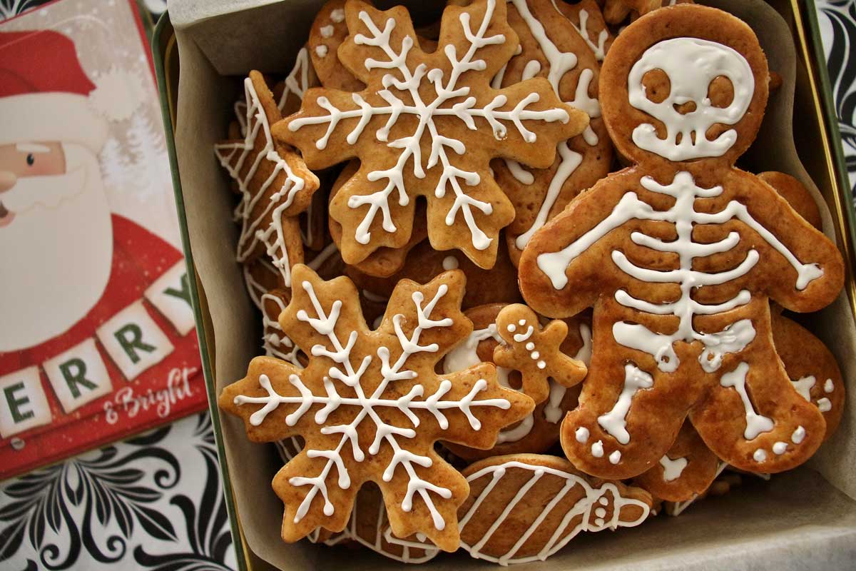 Closeup of a cookie tin filled with gingerbread cookies shaped like snowflakes and skeletons.