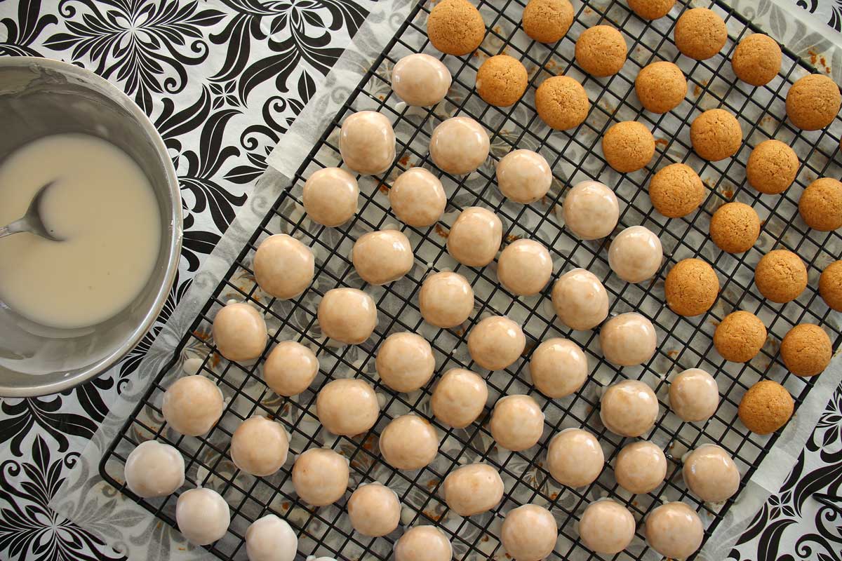 Pfeffernusse cookies on a cooling rack in the process of being glazed.