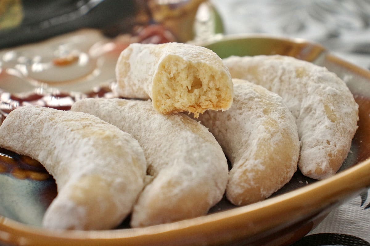 Closeup of a plate of vanilla crescent cookies with a half-eaten cookie on top.