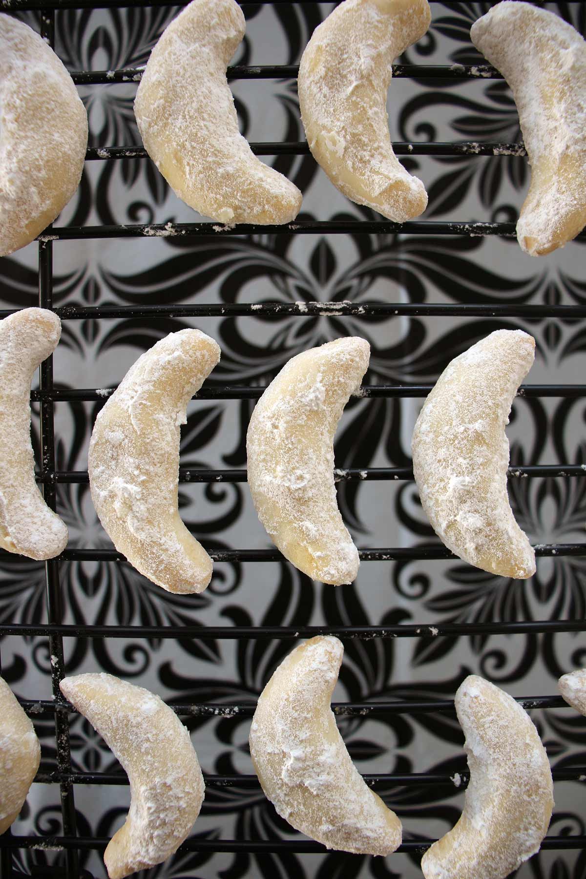 Powdered sugar dusted crescent cookies arranged on a wire cooling rack.