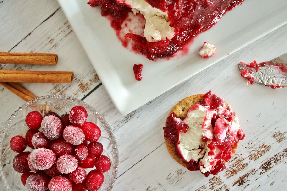 Cranberry cinnamon goat cheese spread on a cracker next to a bowl of frozen cranberries.
