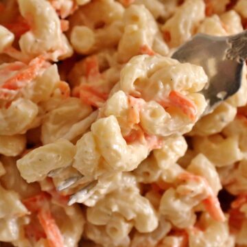 Closeup of a forkful of macaroni salad with grated carrot.