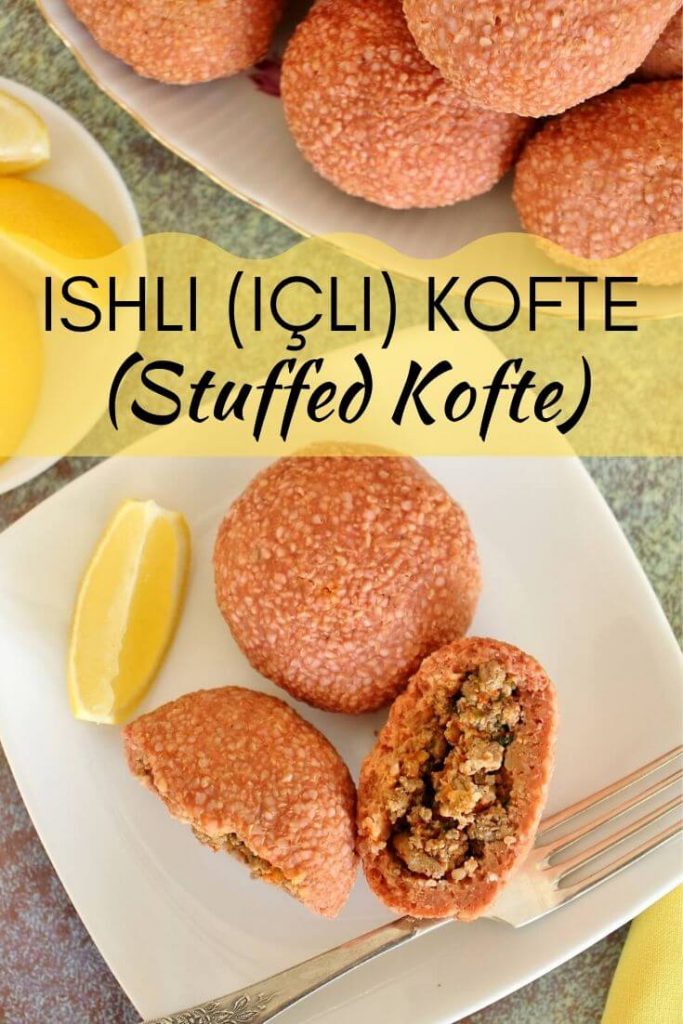2 round ishli koftes on a white square plate, 1 is broken in half to show the filling. There is a lemon wedge on the plate, and a plate of lemon wedges and platter of more koftes next to the plate.
