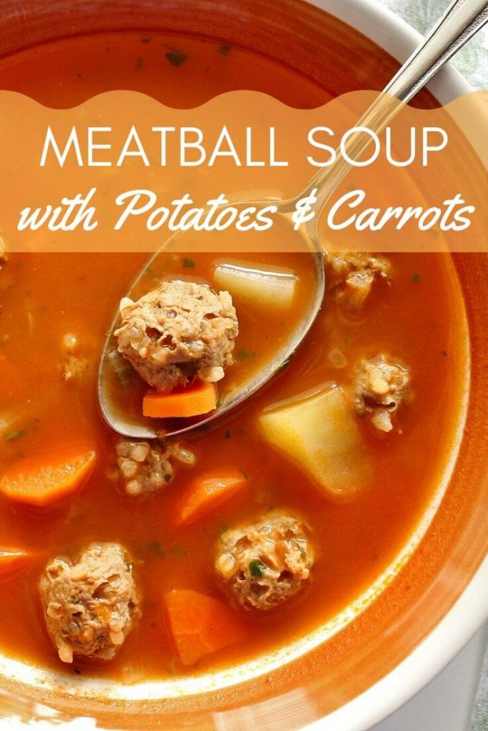 Meatball soup with potatoes and carrots in a bowl, with a spoon holding some soup over the bowl's surface