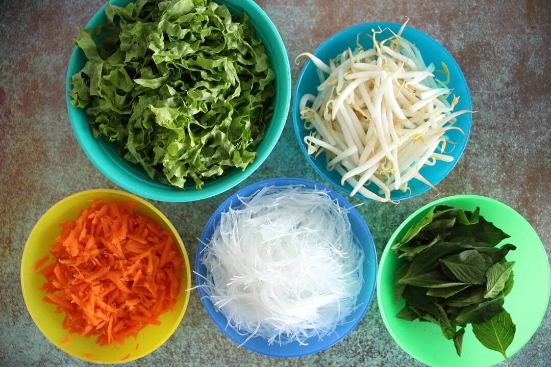 Bowls of ingredients for Nime Chow (lettuce, bean sprouts, grated carrots, cellophane noodles, fresh basil)