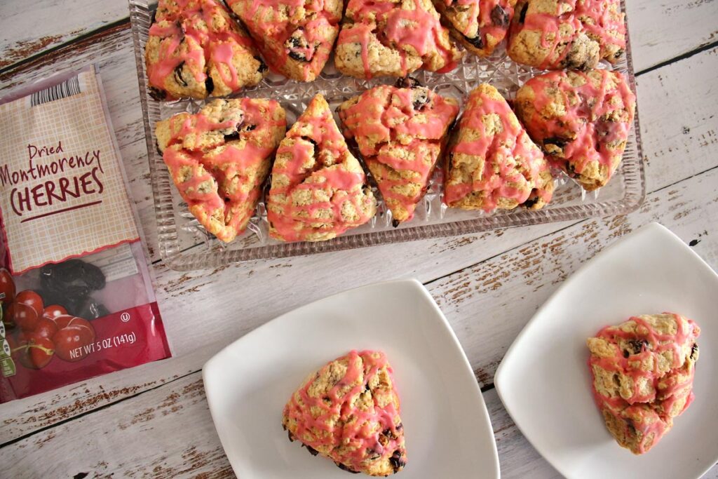 A platter of tipsy cherry scones, and 2 scones on individual plates, with a bag of dried cherries to the side