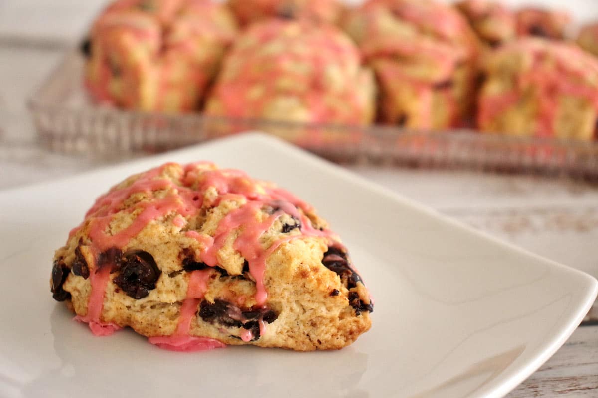 Closeup of a cherry scone drizzled with pink glaze on a white square plate.