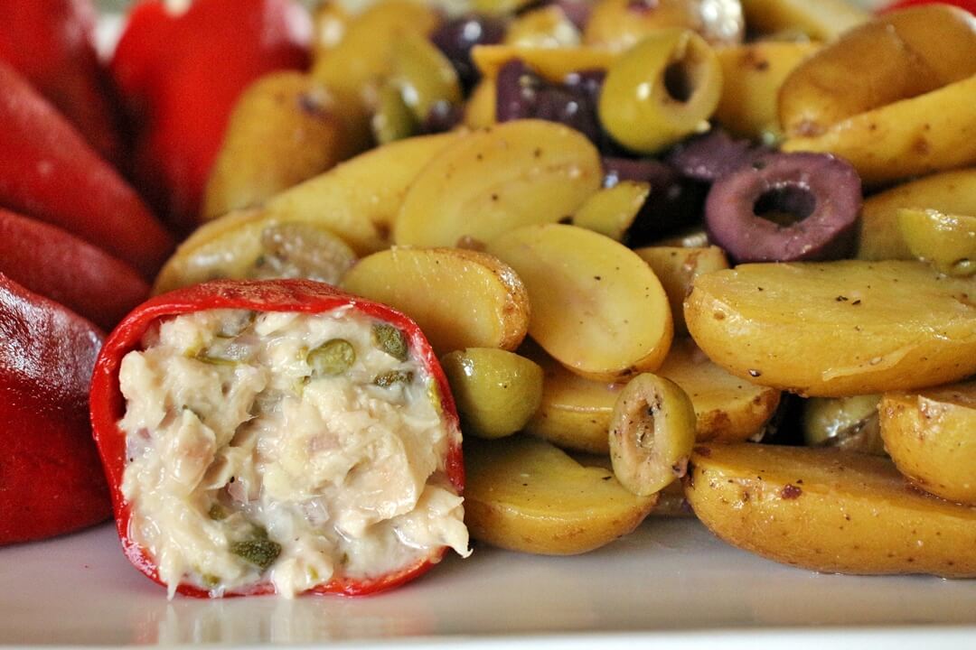 Close up view of a piquillo pepper stuffed with tuna salad, next to a pile of halved fingerling potatoes and chopped olives