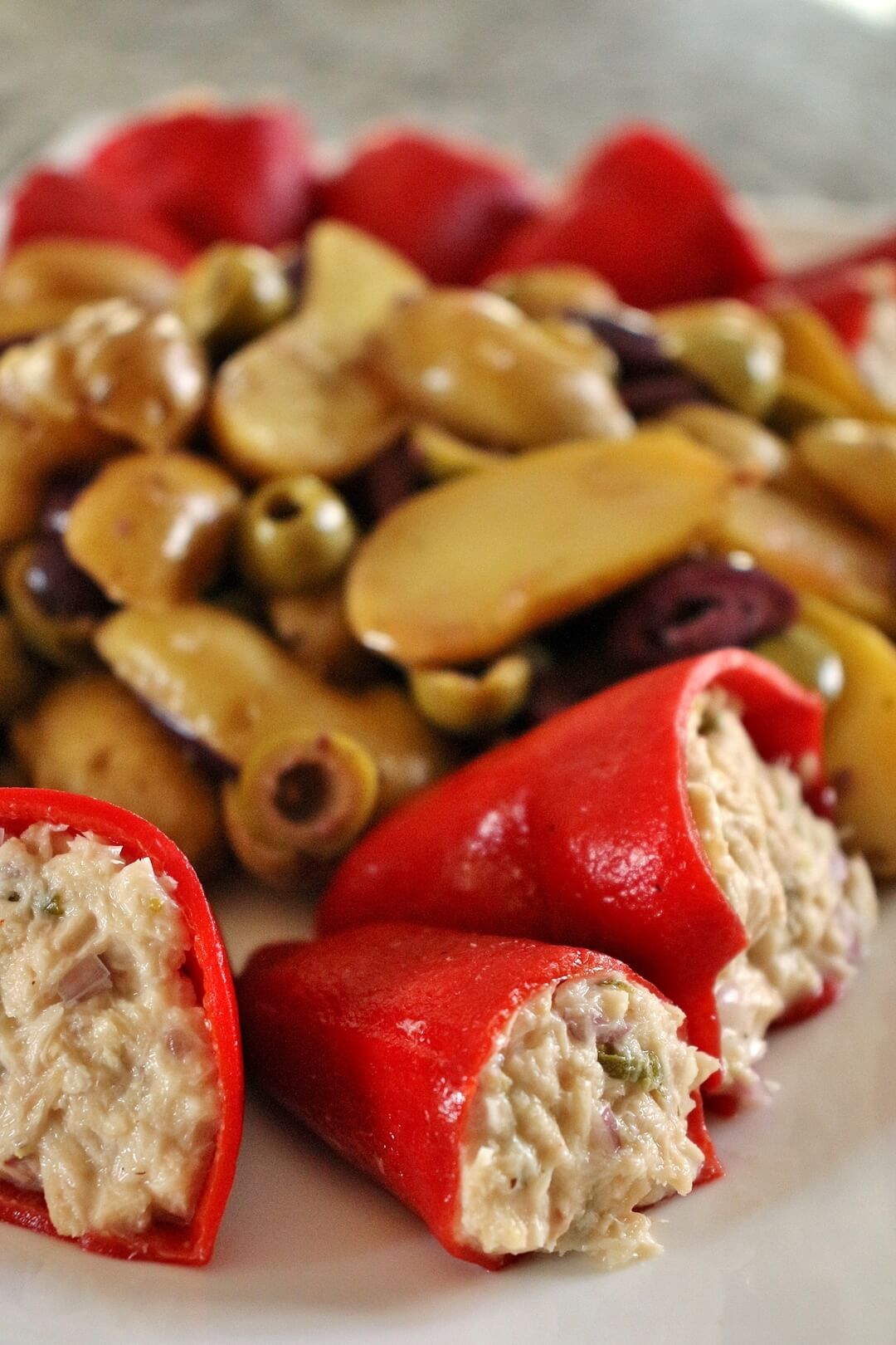 Close up of 3 piquillo peppers stuffed with tuna salad, with potato and olive salad