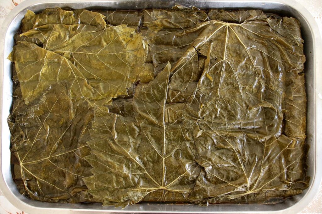 A baking pan full of stuffed grape leaves, covered with a layer of grape leaves spread out like a blanket