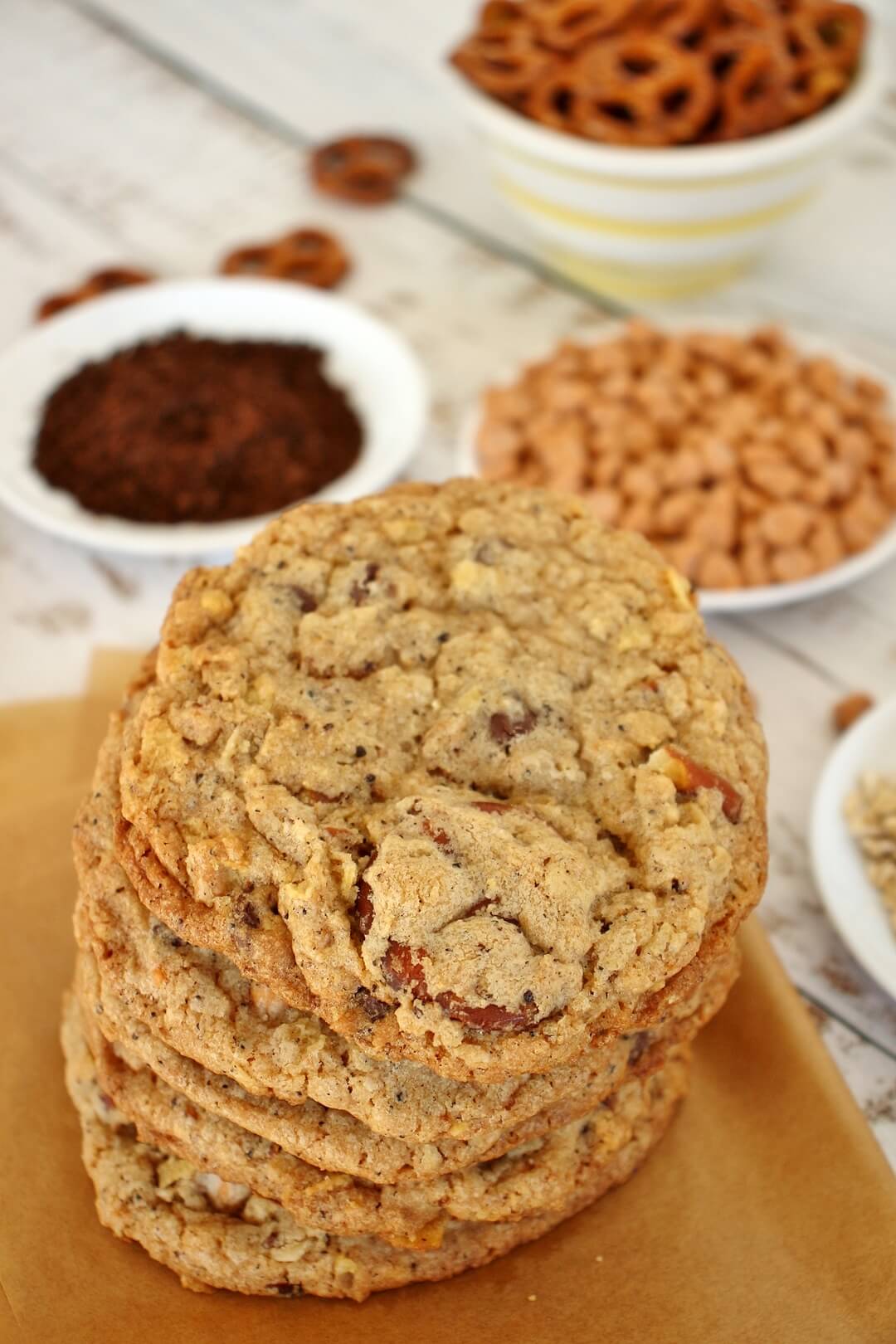 a stack of compost cookies on a piece of parchment paper surrounded by ingredient bowls