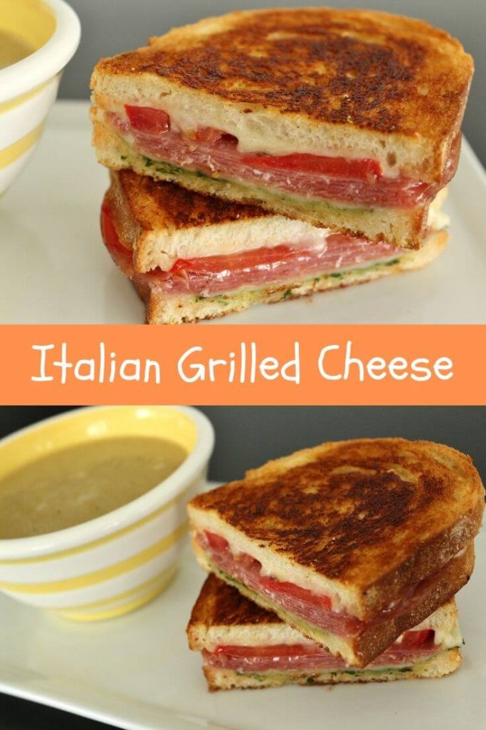 A grilled cheese with salami, tomato, and pesto on a white plate with a cup of soup in a white and yellow striped bowl.
