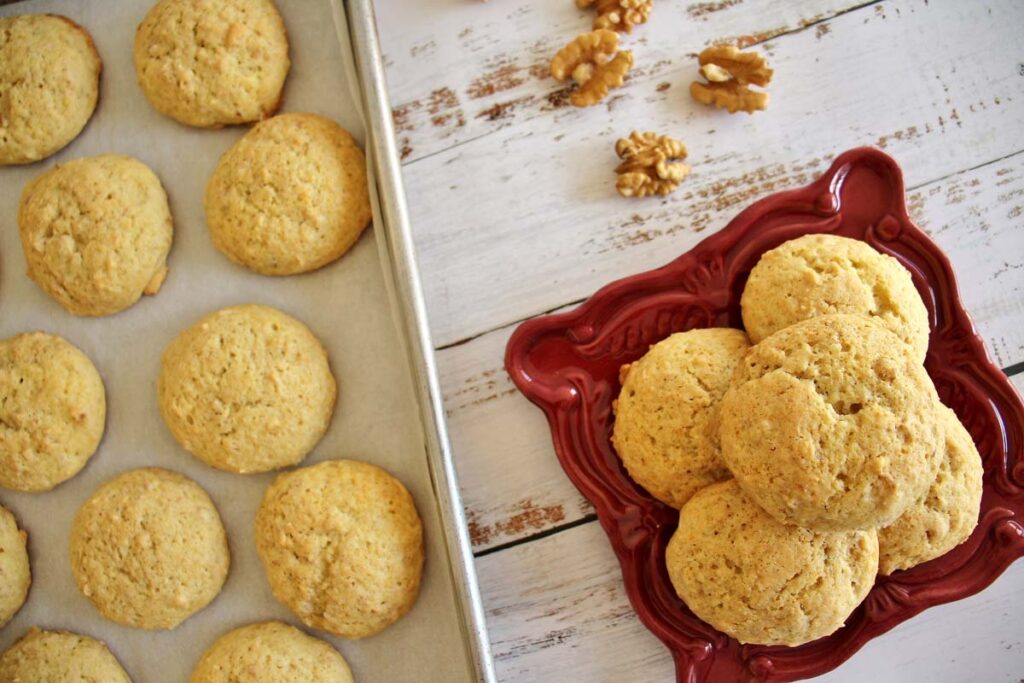 Five cakey yogurt cookies on a square dark red plate, with a tray of cookies to the side