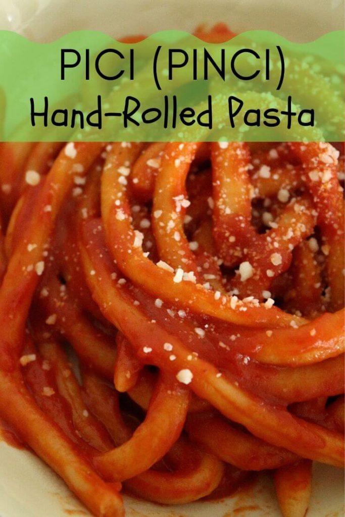 Closeup of hand-rolled pici pasta in tomato sauce, topped with grated cheese
