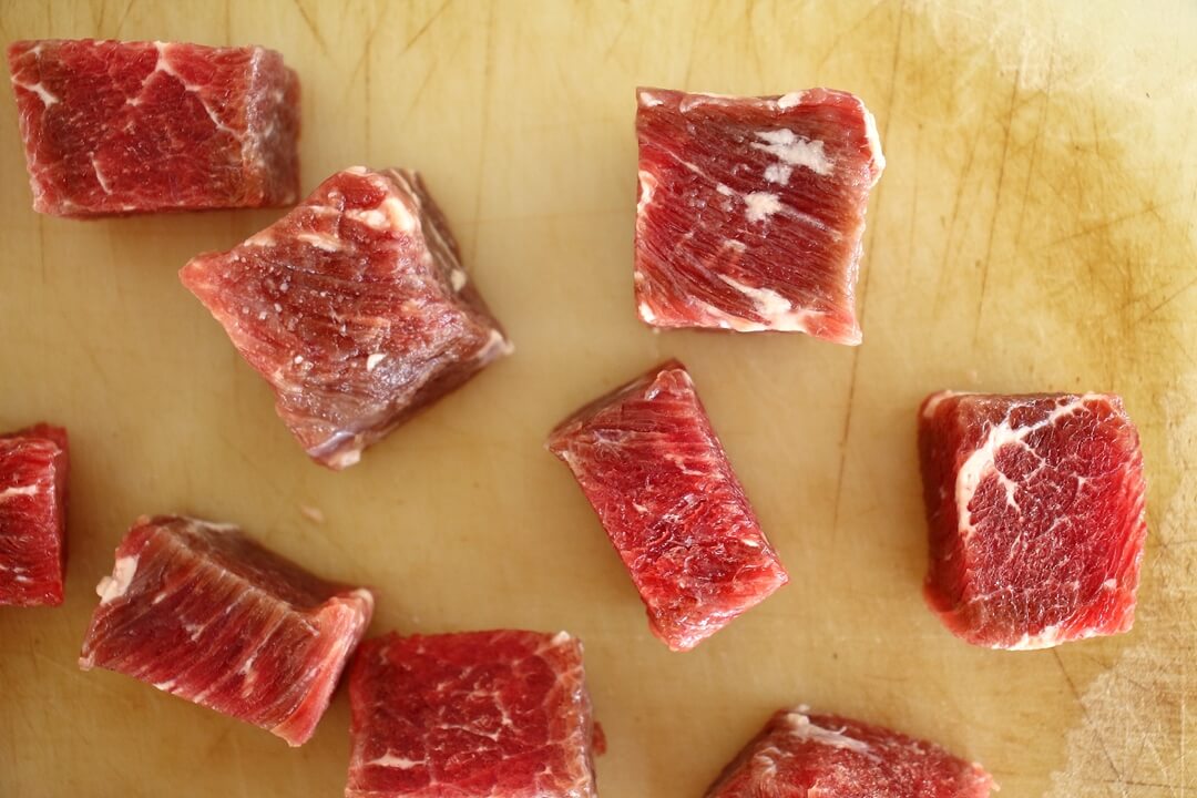 Cubed raw steak on a cutting board.
