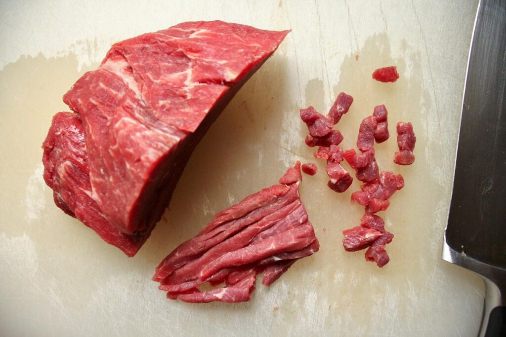 Hand-chopping beef tenderloin on a white cutting board