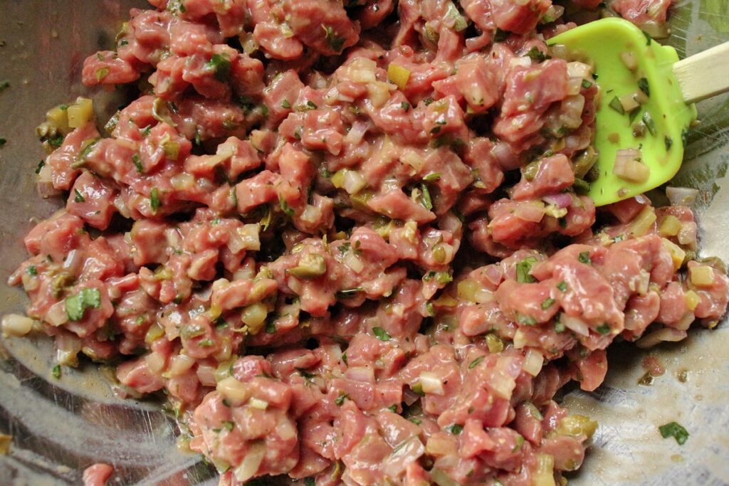 Steak tartare mixture in a metal mixing bowl