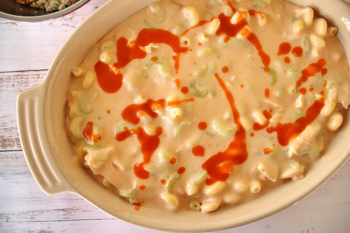 Buffalo chicken mac and cheese (unbaked) in oval baking dish, drizzled with buffalo sauce