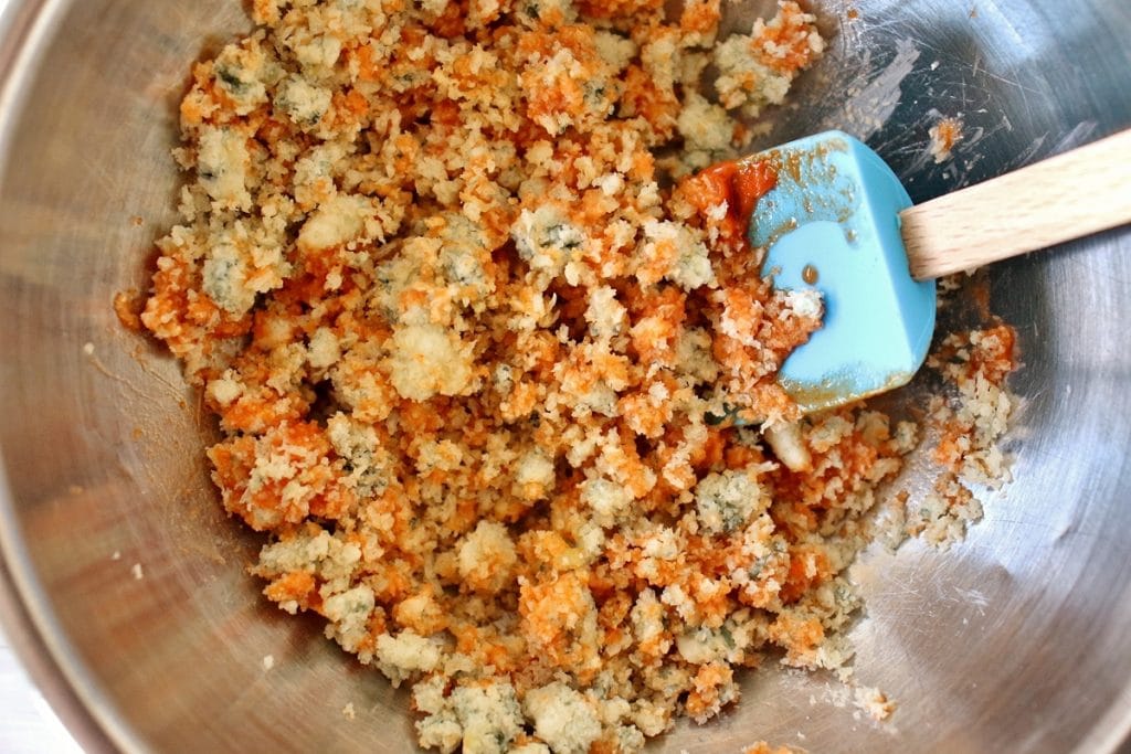 A mixture of panko, garlic, blue cheese, and buffalo sauce in a mixing bowl with a blue spatula in the bowl