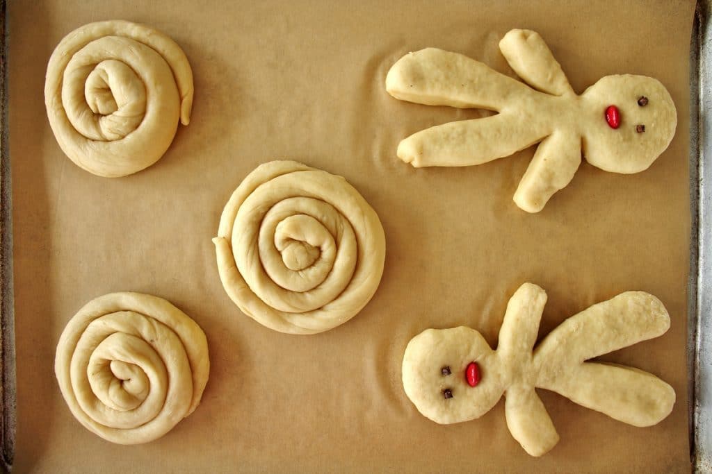 A baking sheet with 3 spiral shaped choreks and 2 small person-shaped choreks, prior to baking
