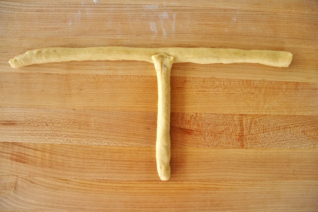Ropes of dough shaped like the letter T on a wooden cutting board