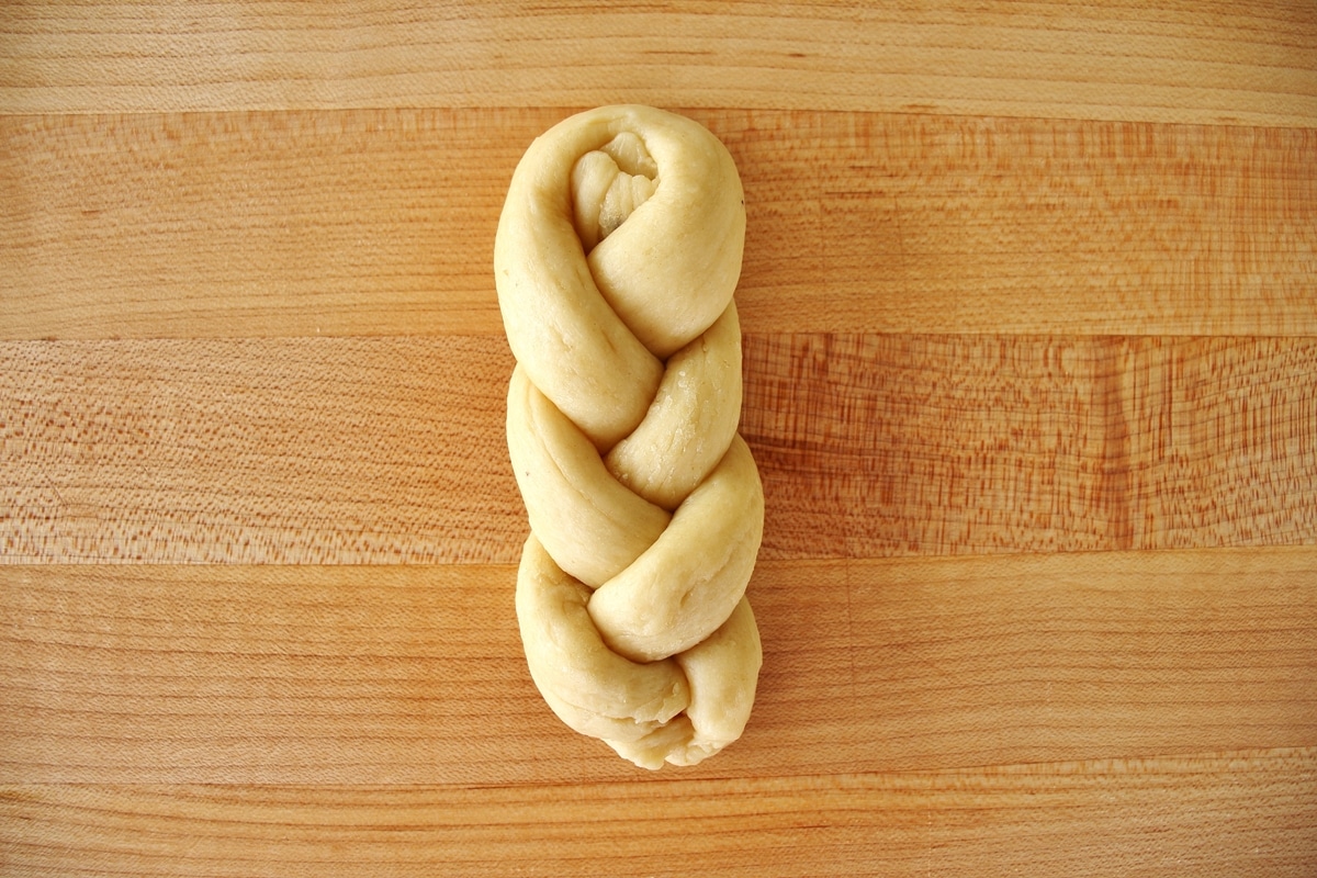 Braided dough on a wooden cutting board.