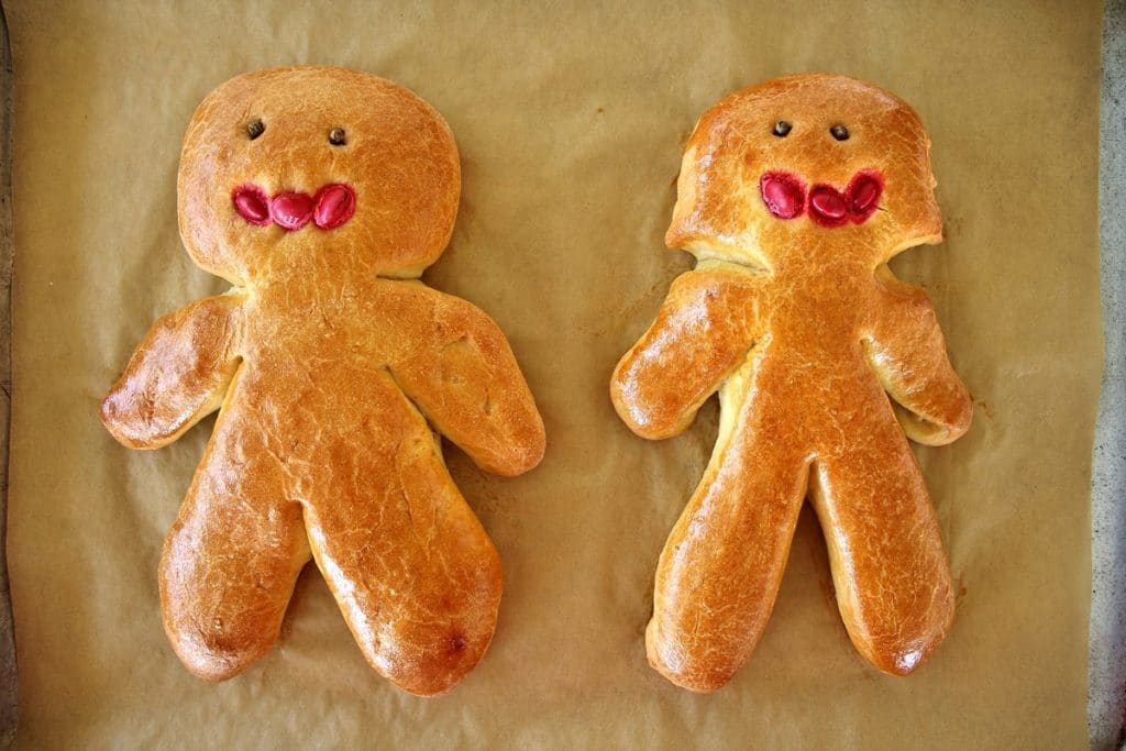 A man and woman chorek person on a parchment lined baking sheet, with whole cloves for eyes and red m&ms for mouths, after baking