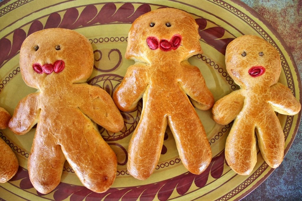 Armenian sweet bread (chorek) shaped like people with whole cloves as eyes, and red m&ms for mouths, displayed on an oval platter