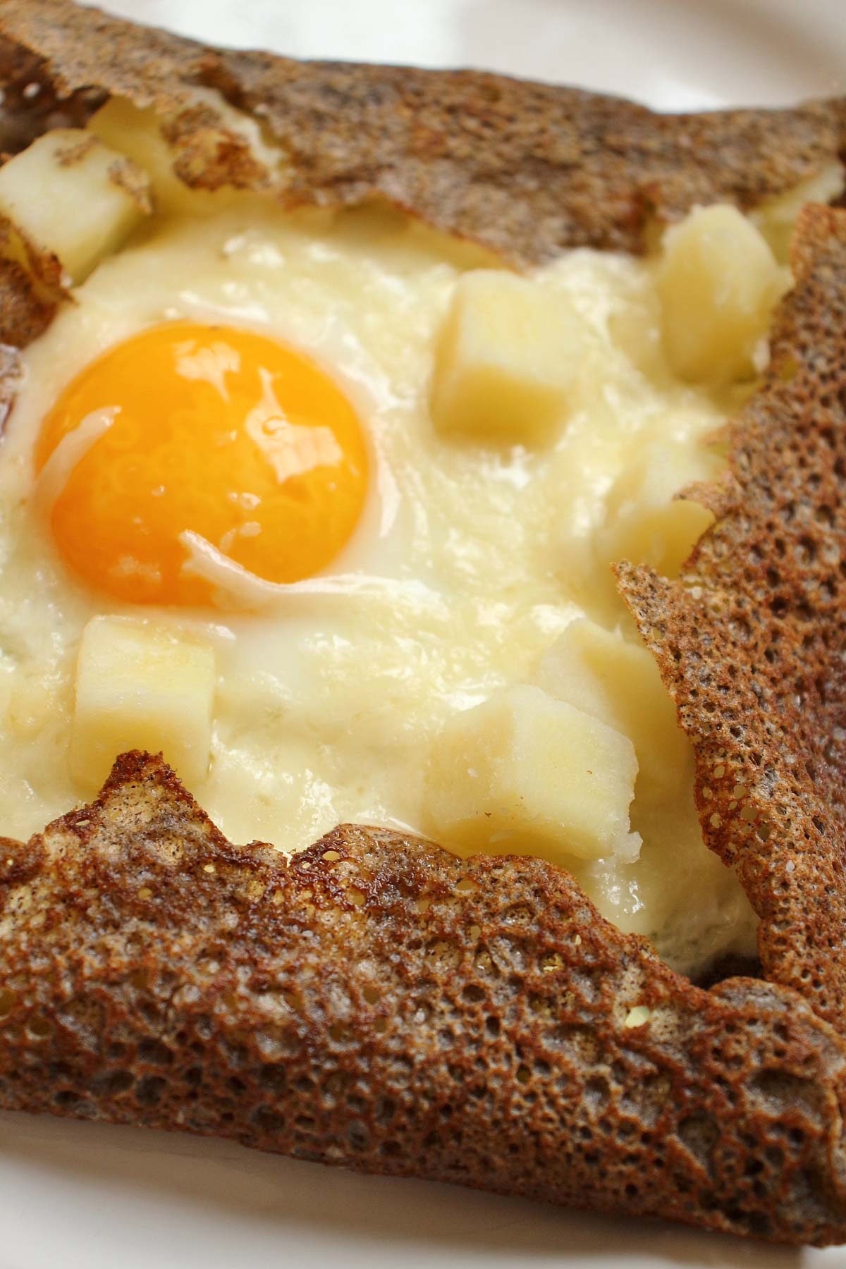 Closeup of a buckwheat galette (crepe) filled with potatoes, cheese, and fried egg